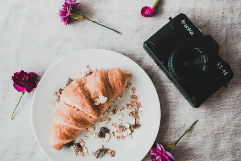 Black dslr camera with croissant in a plate 